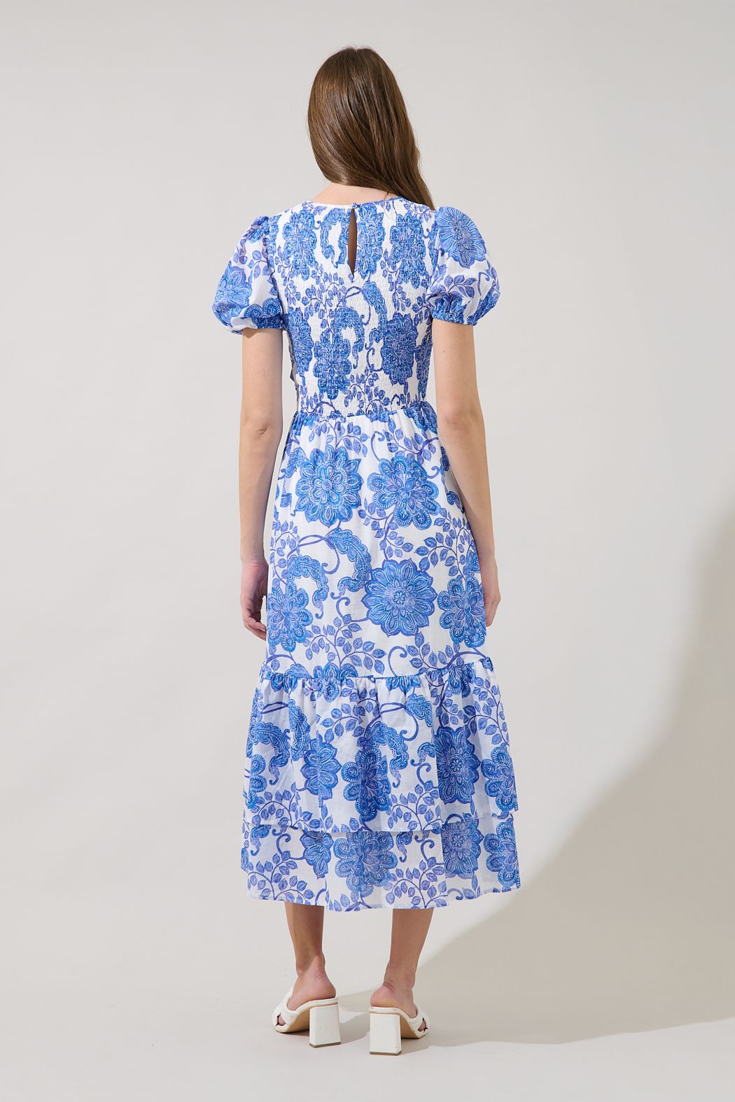 Back view of Sugarlips Aruba blue floral smocked midi dress featuring puff sleeves, back keyhole, and tiered skirt.