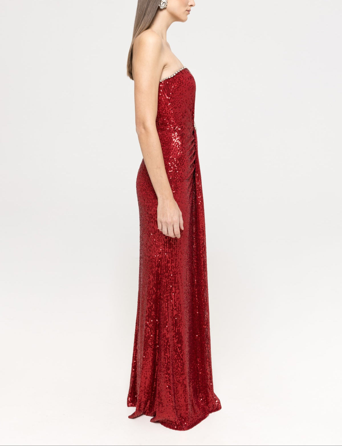 Model is wearing a strapless red sequin maxi dress with a straight neckline trimmed with crystals and a fitted silhouette, emphasizing the shimmering fabric.