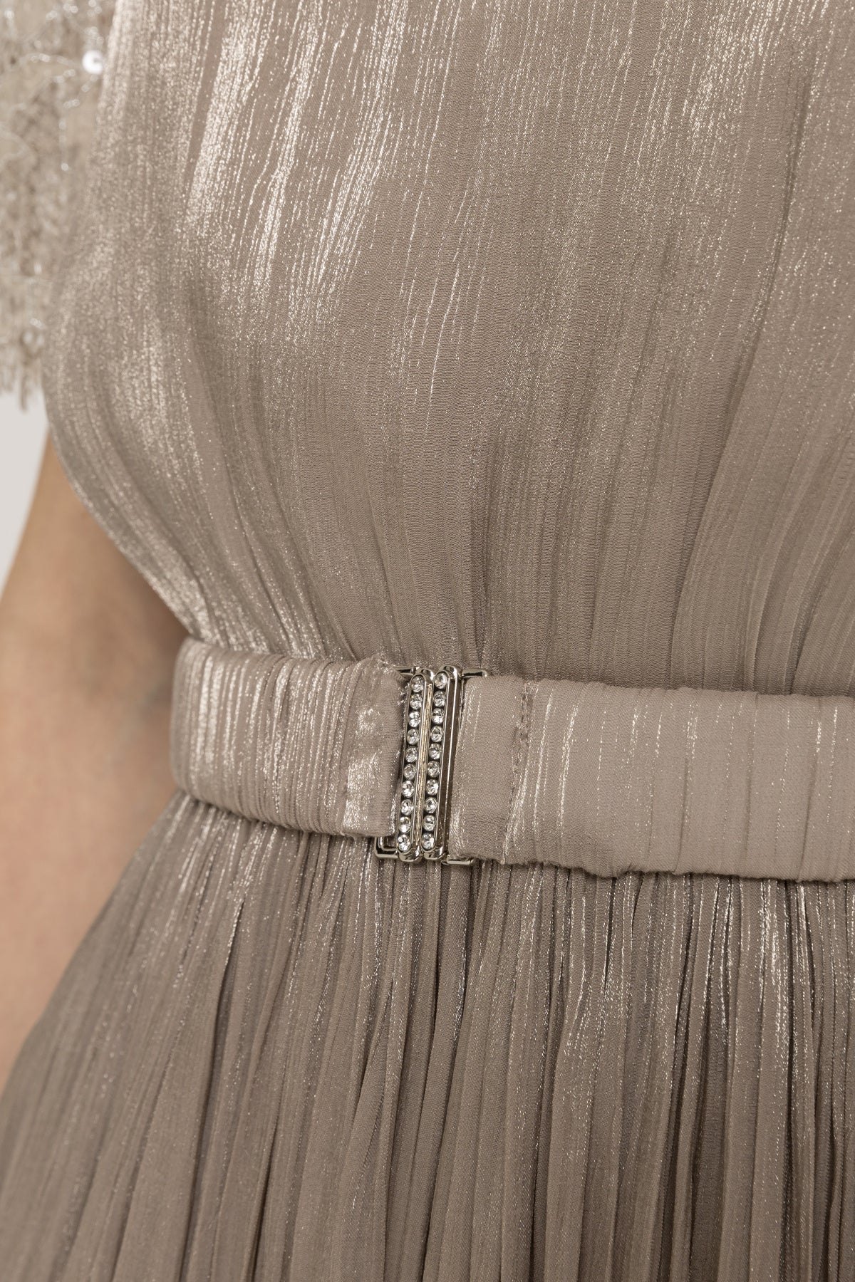 Close-up of champagne fabric belt with crystal buckle on a metallic pleated midi dress