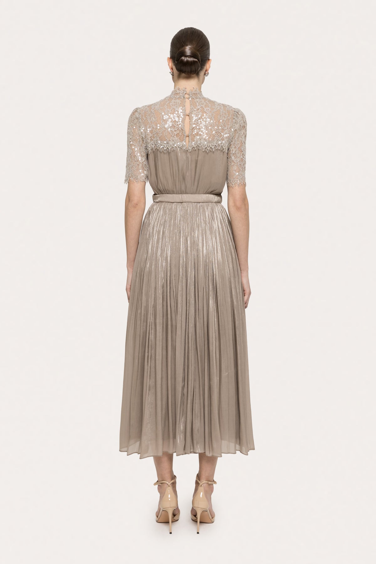 Back view of a champagne lace and metallic pleated midi dress with high neckline and belted waist