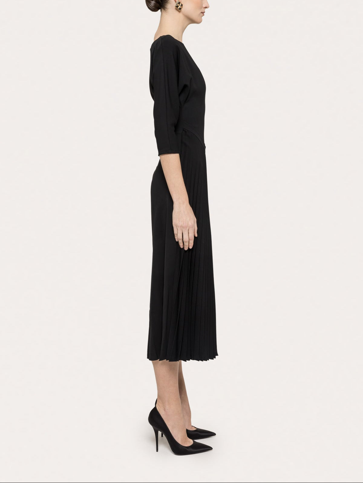 Side view of black pleated midi dress with structured bodice and three-quarter sleeves
