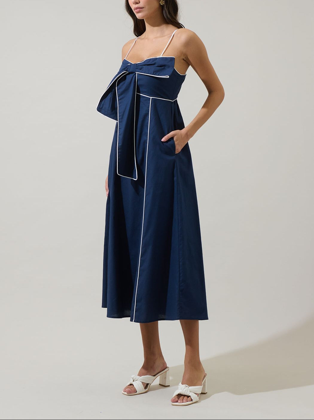 Three-quarter view of the Viona navy midi dress with oversized bow, white piping, A-line skirt and side pockets.