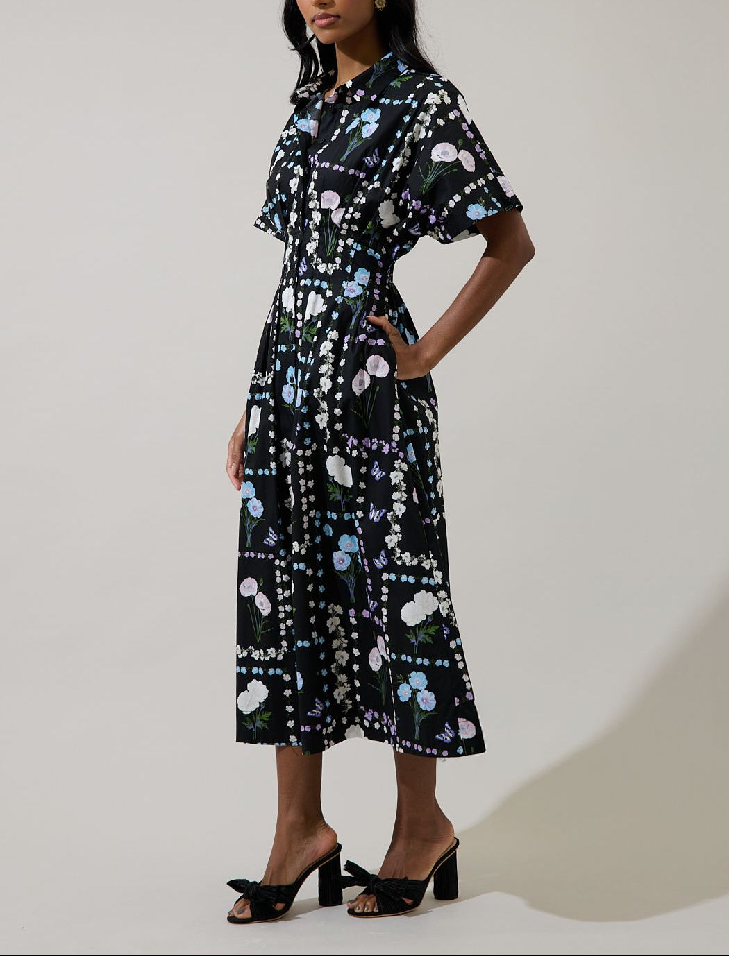 Side view of black pastel floral midi shirt dress with button front, pockets and pleated skirt