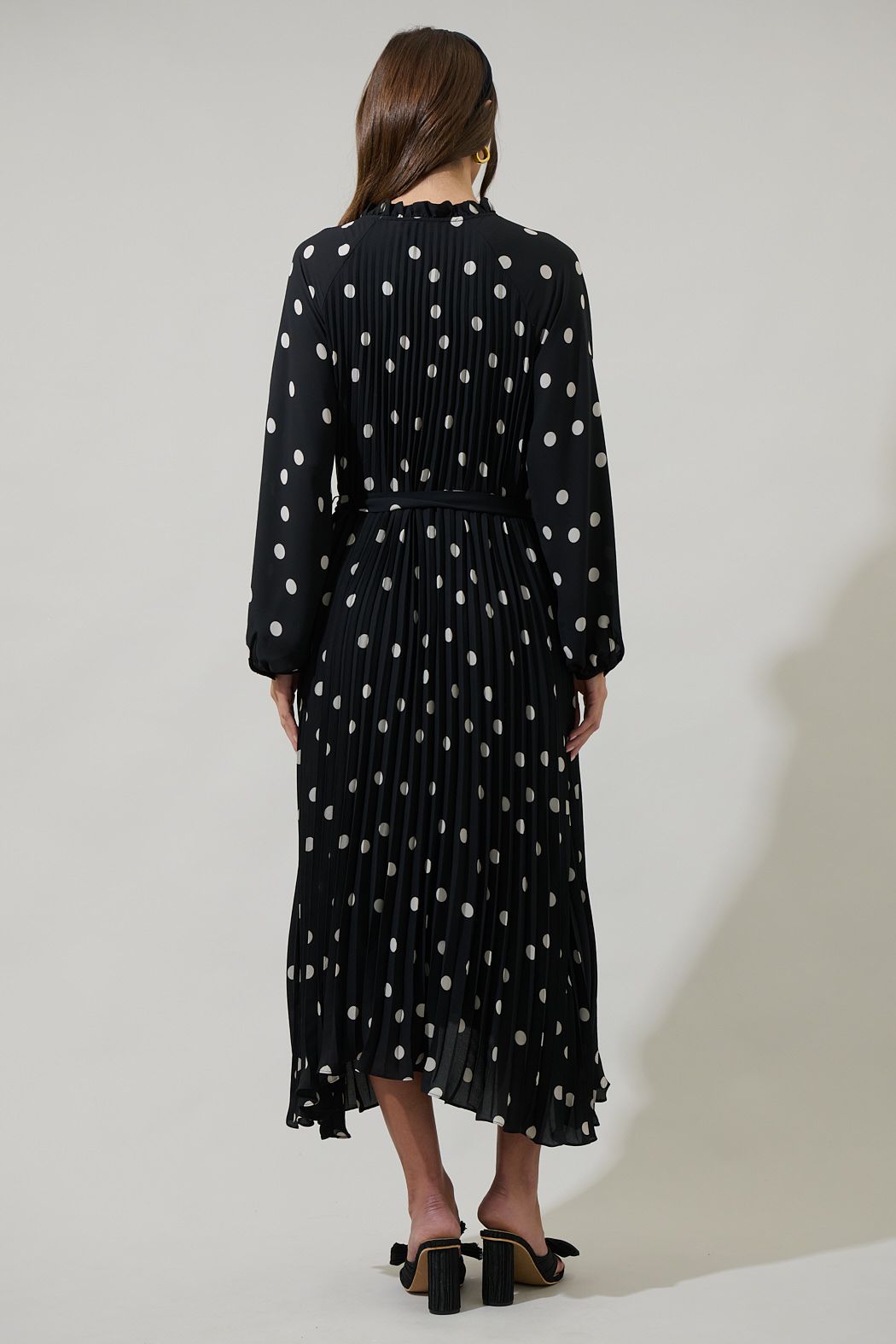 Back view of black polka dot pleated midi dress with long sleeves and flowing skirt