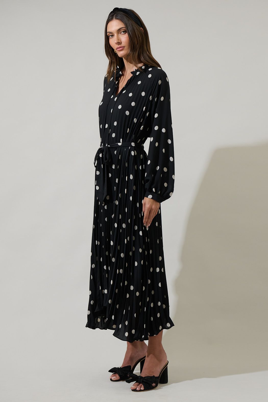 Side view of black and ivory polka dot midi dress with pleated skirt and long sleeves