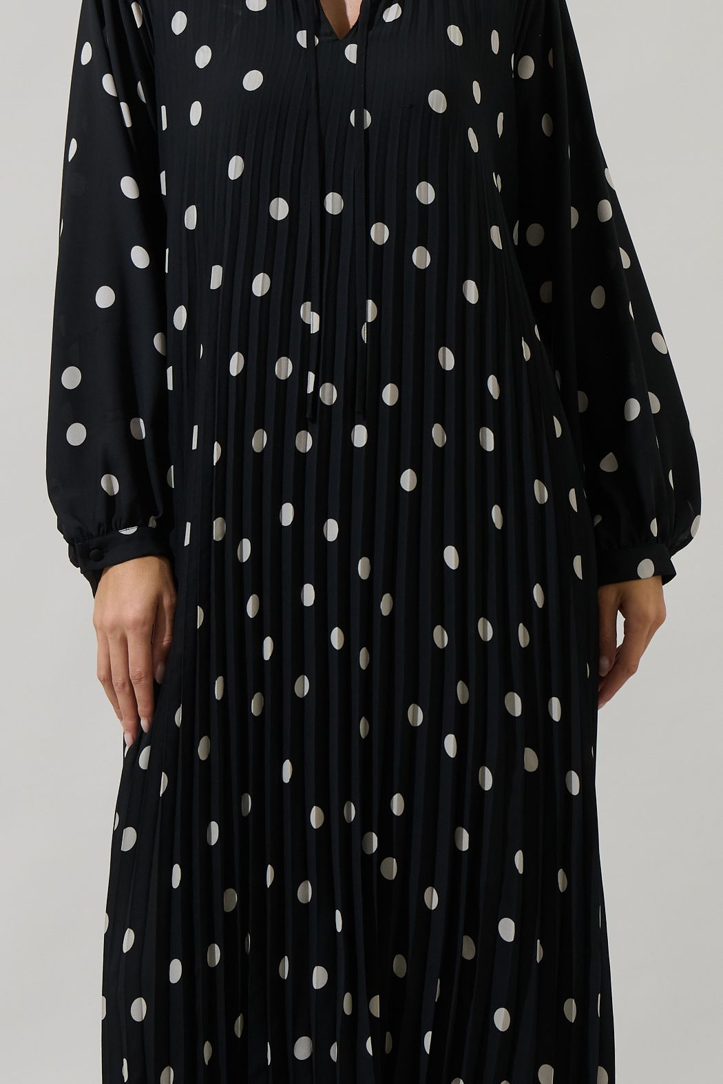 Close-up of black polka dot pleated midi dress with split neckline and long sleeves