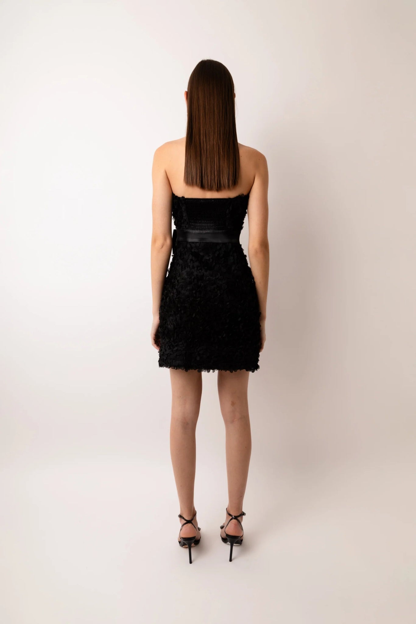 Back view of black bandeau mini dress with textured fabric and waist bow detail