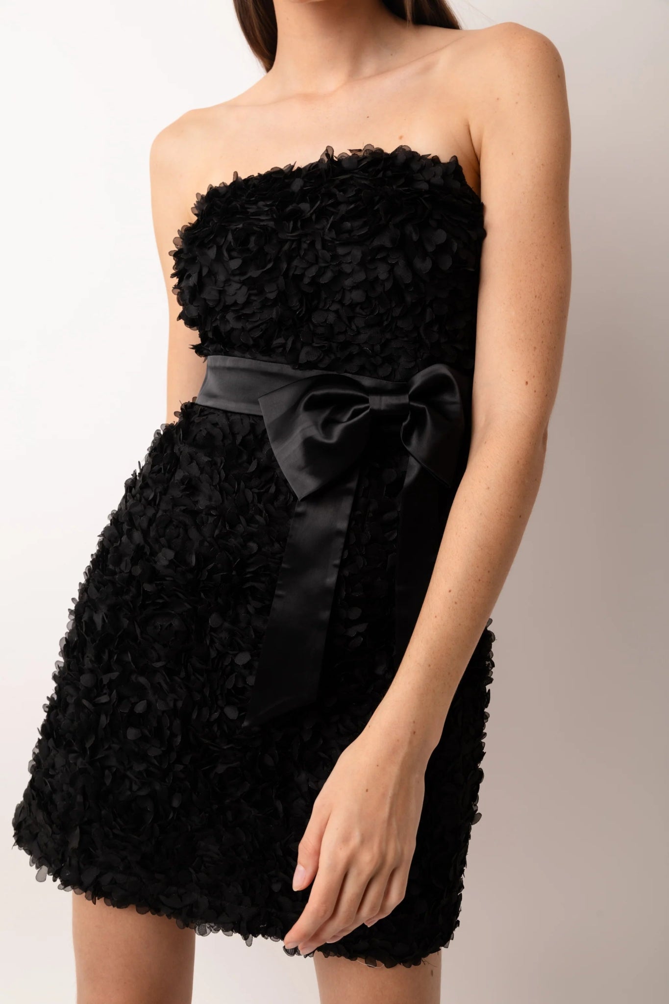 Close-up of black textured strapless mini dress with satin bow detail at waist
