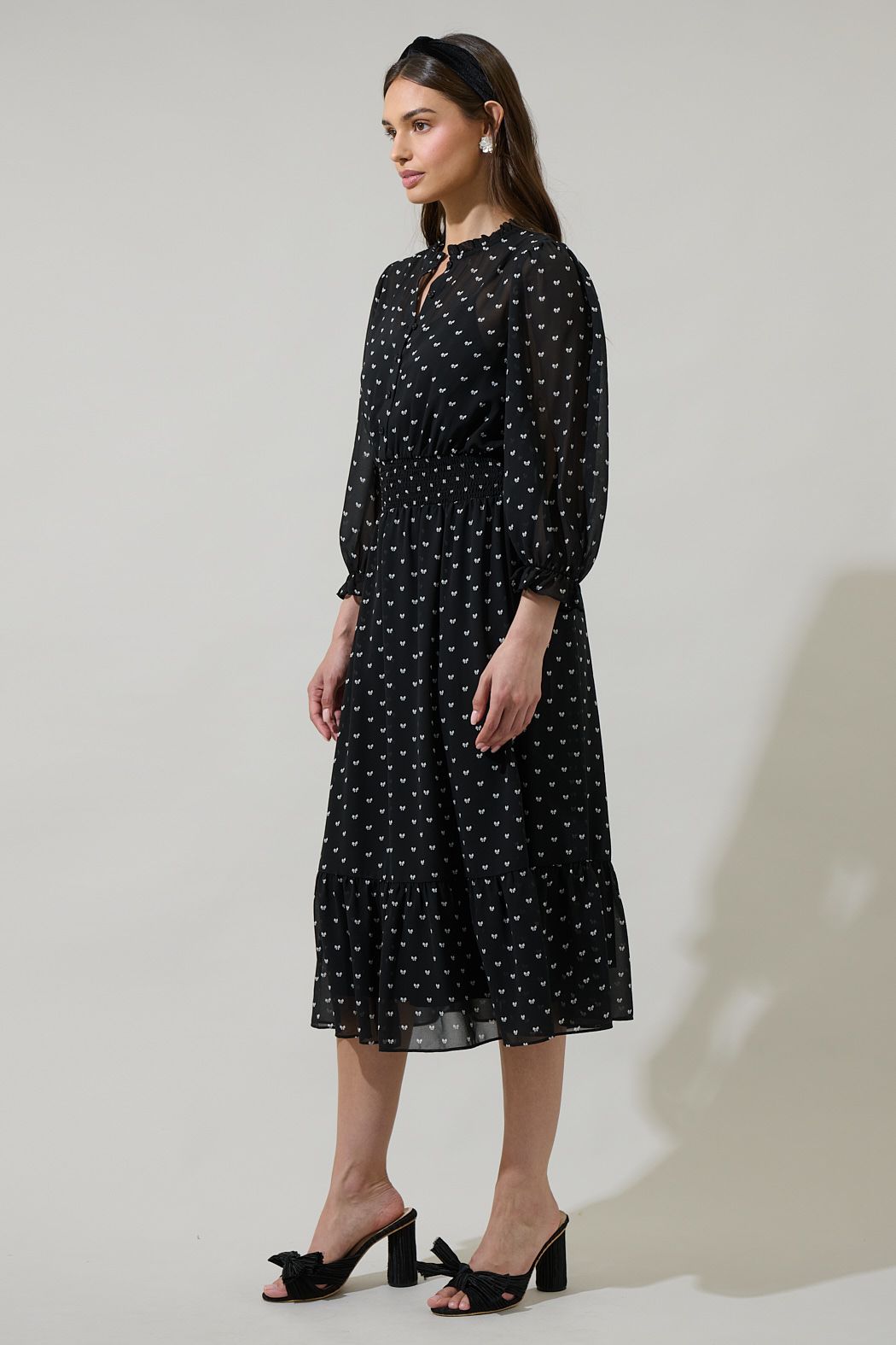 Side view of black and white bow print midi dress with sheer sleeves and ruffle hem