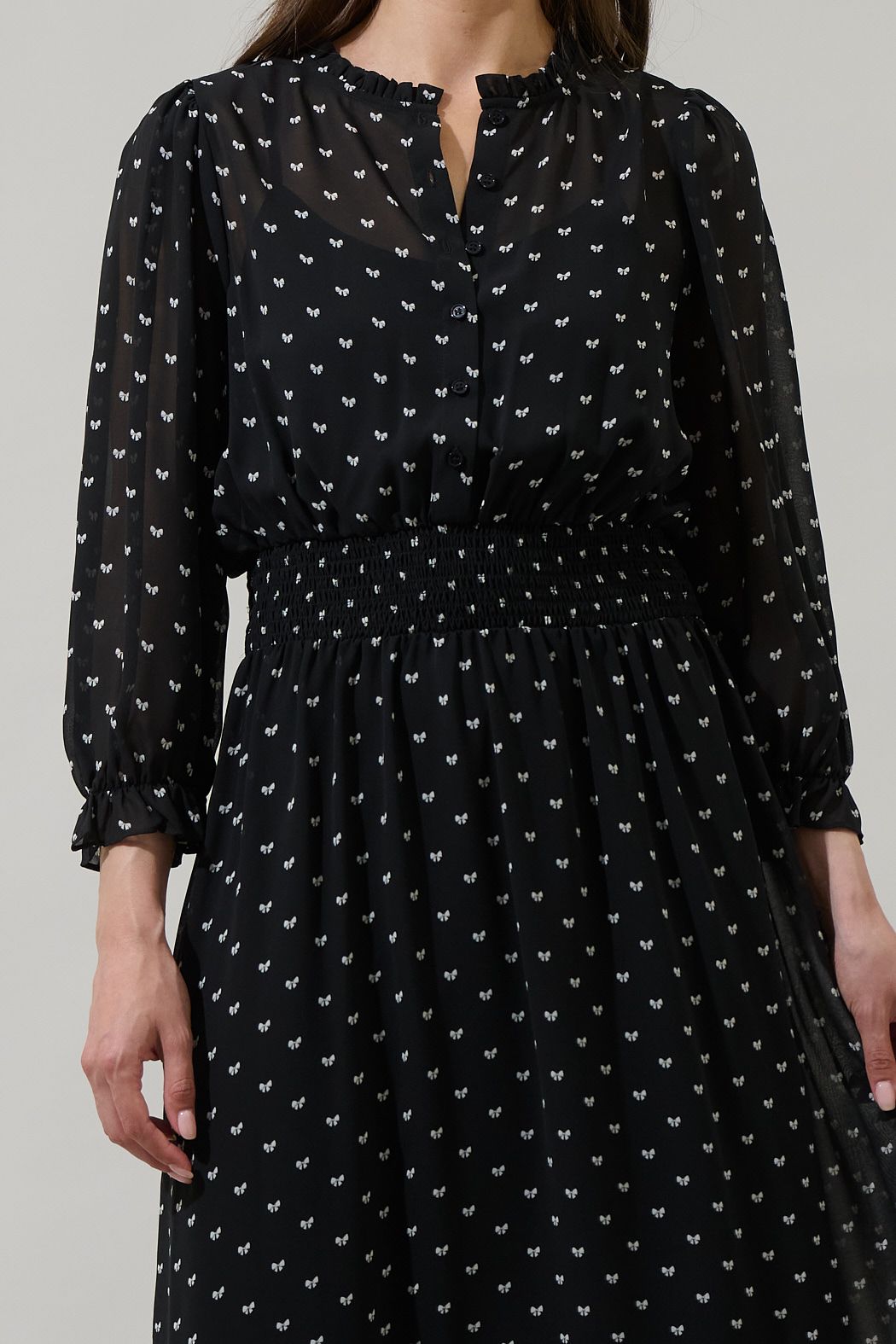 Close-up of black bow print dress with ruffled split neckline, button placket, and smocked waist