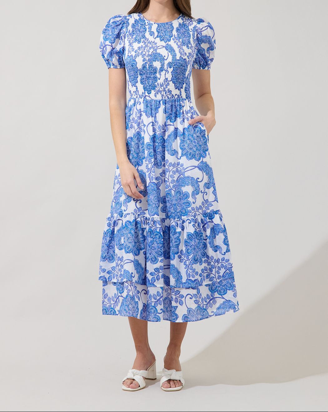 Sugarlips Aruba blue floral smocked midi dress with puff sleeves, pockets, round neckline, and tiered skirt on model.