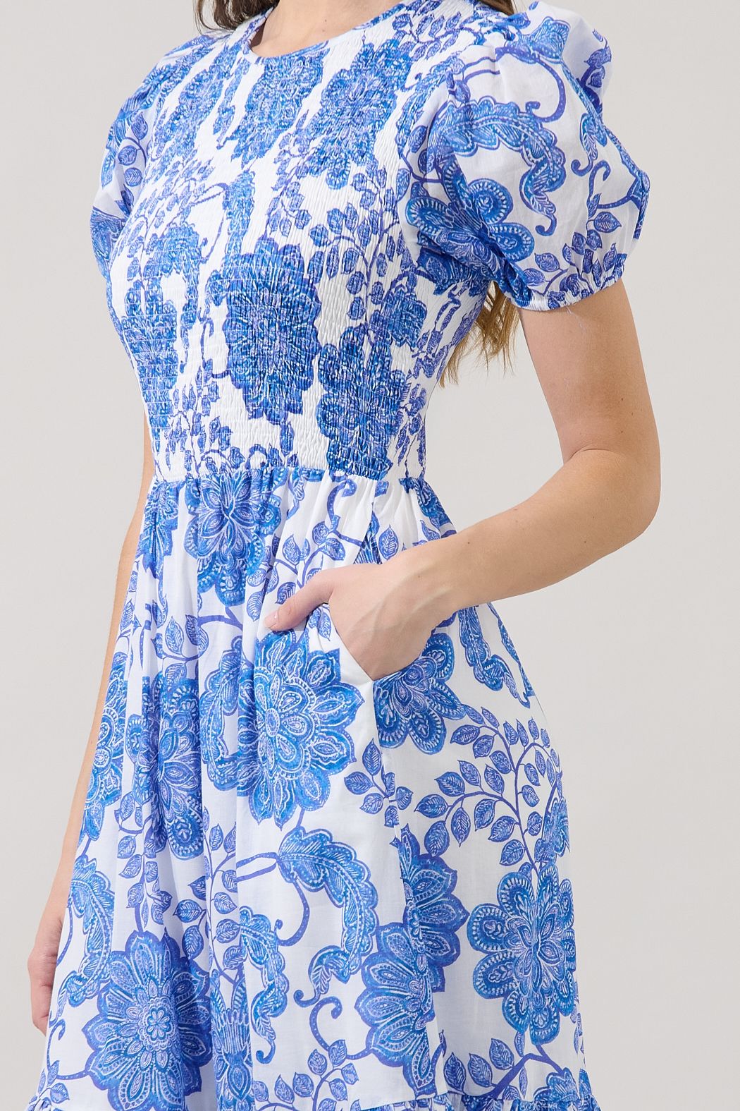 Close-up of blue and white floral Sugarlips smocked midi dress showing puff sleeve, elastic bodice, pocket, and porcelain print.