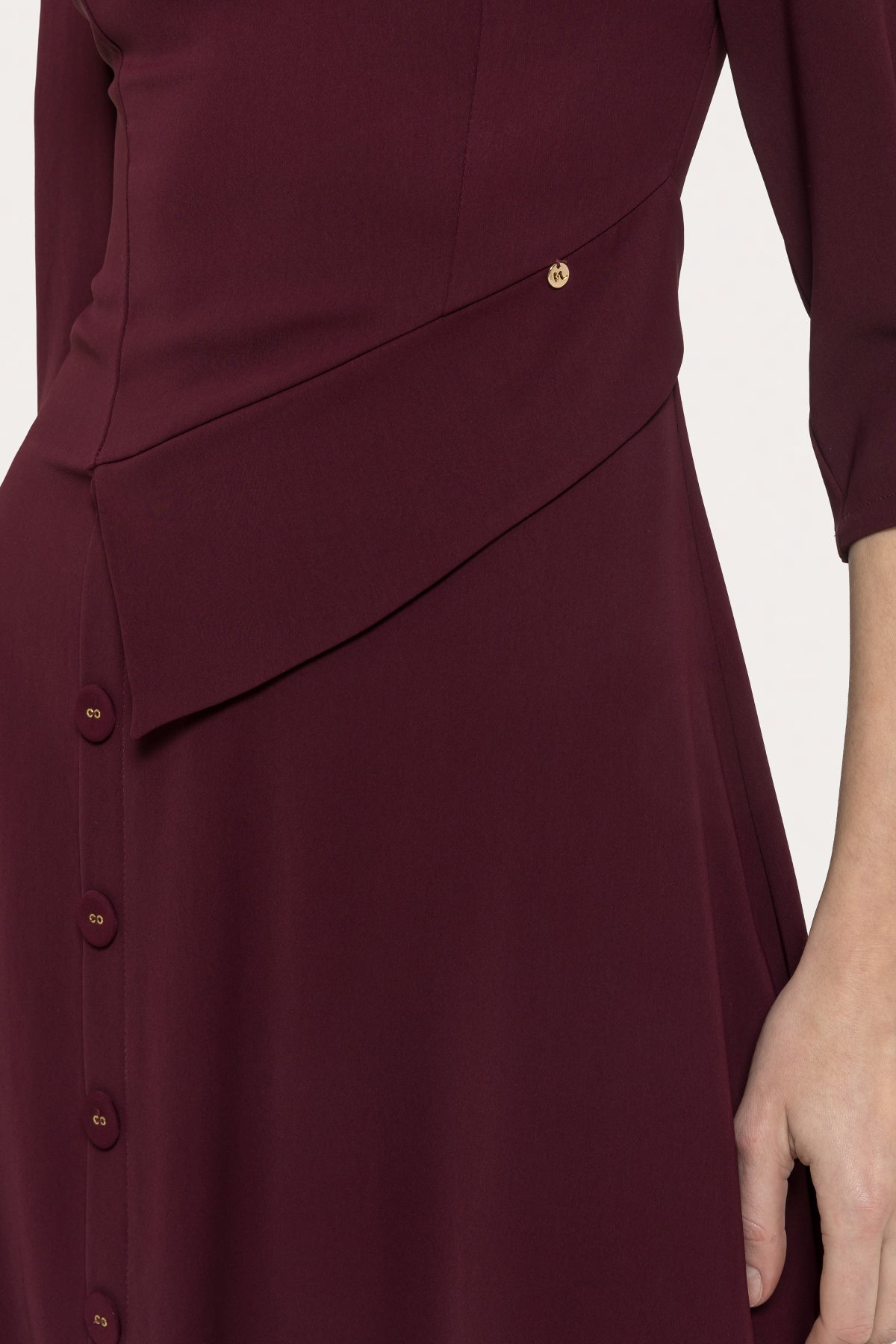 Close-up of bordeaux midi dress showing asymmetric waist flap, front buttons and gold-tone accent