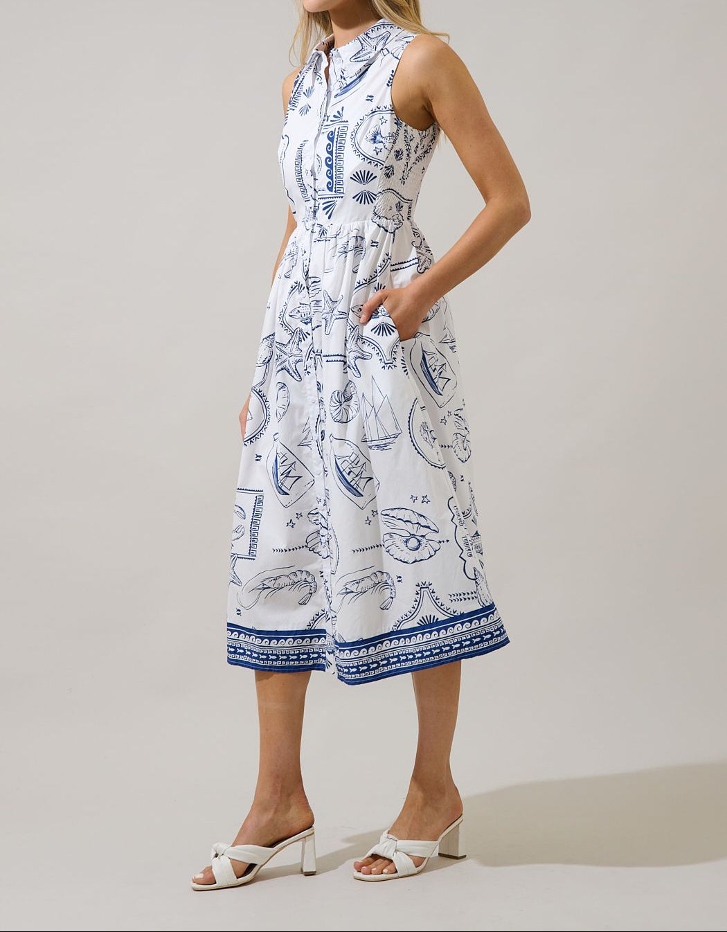 Side view of white and navy seaside print sleeveless midi shirtdress with pockets