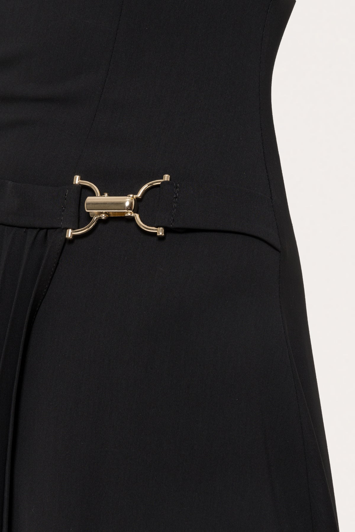Close-up of gold tone metallic waist detail on black pleated-panel midi dress