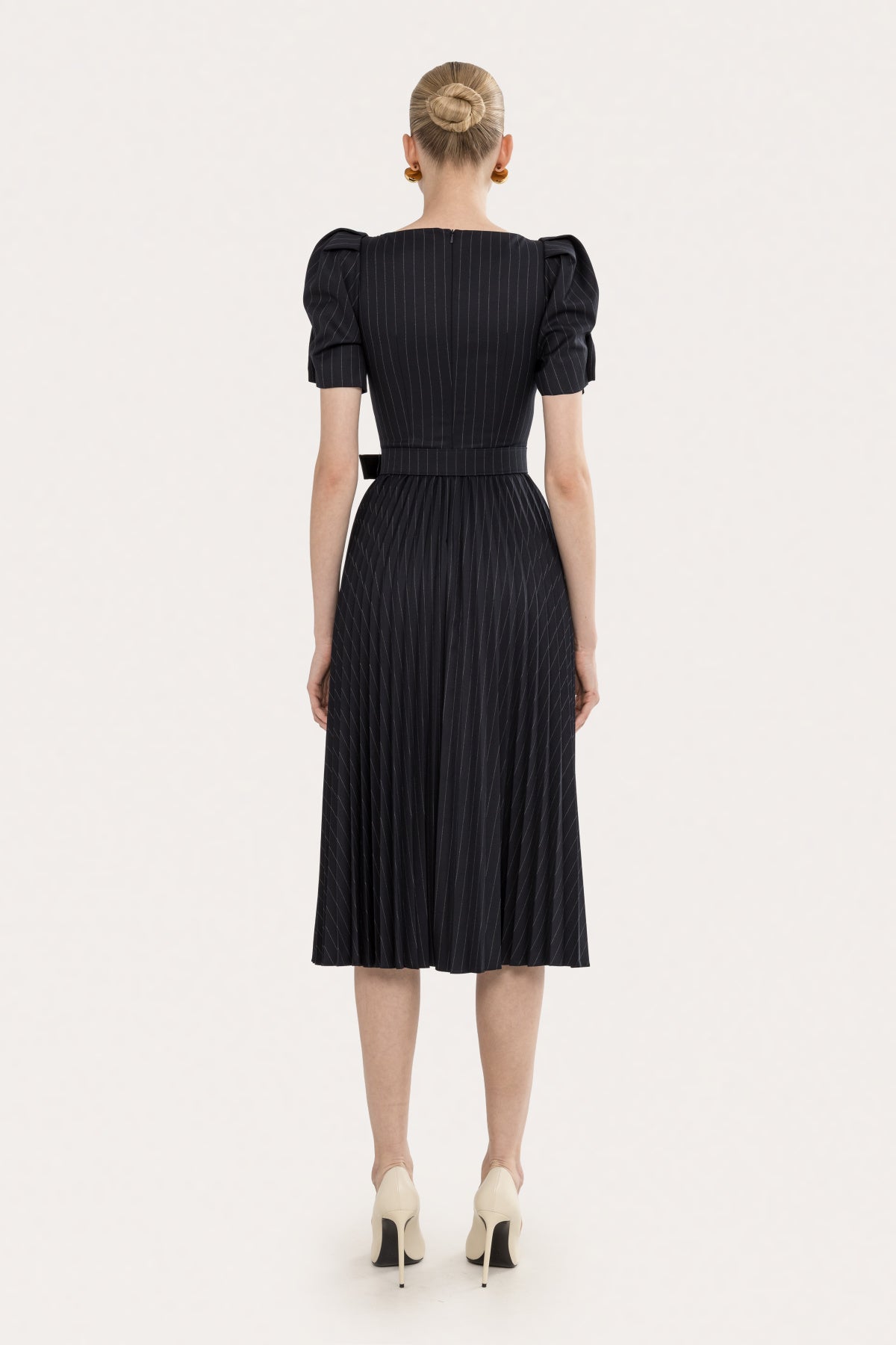 Back view of a black pinstripe pleated midi dress with puff sleeves, belted waist, and midi-length skirt