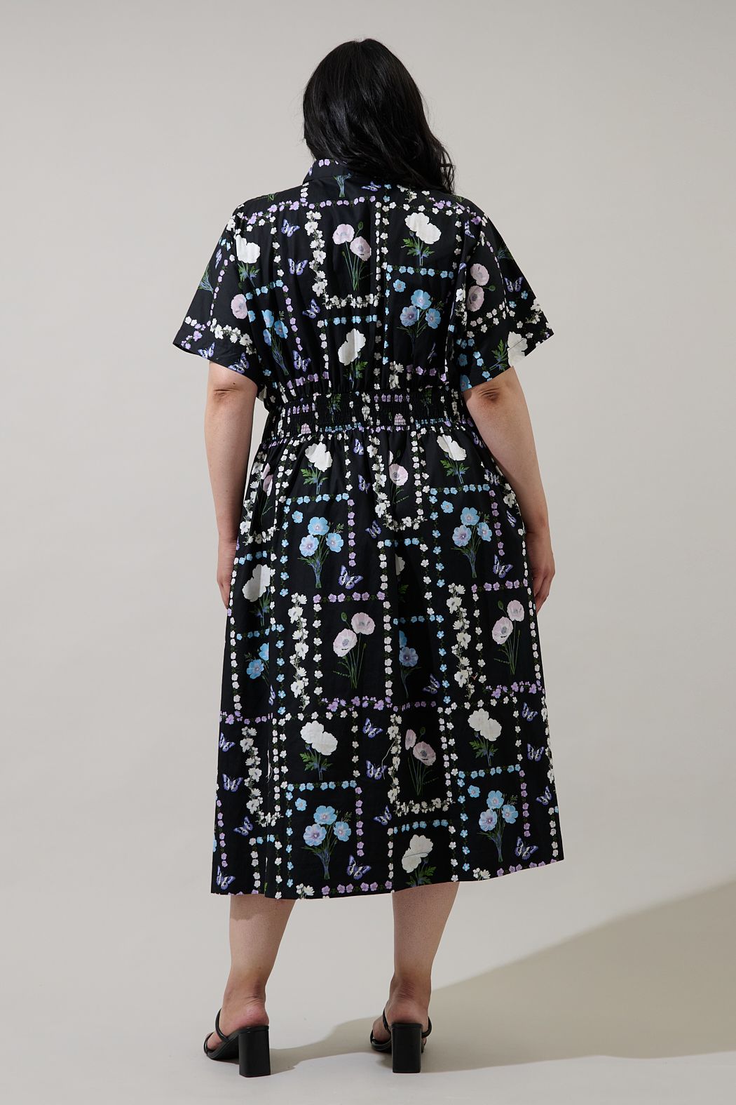 Curve fit back view of black floral pleated midi dress with elastic smocked waist and short sleeves