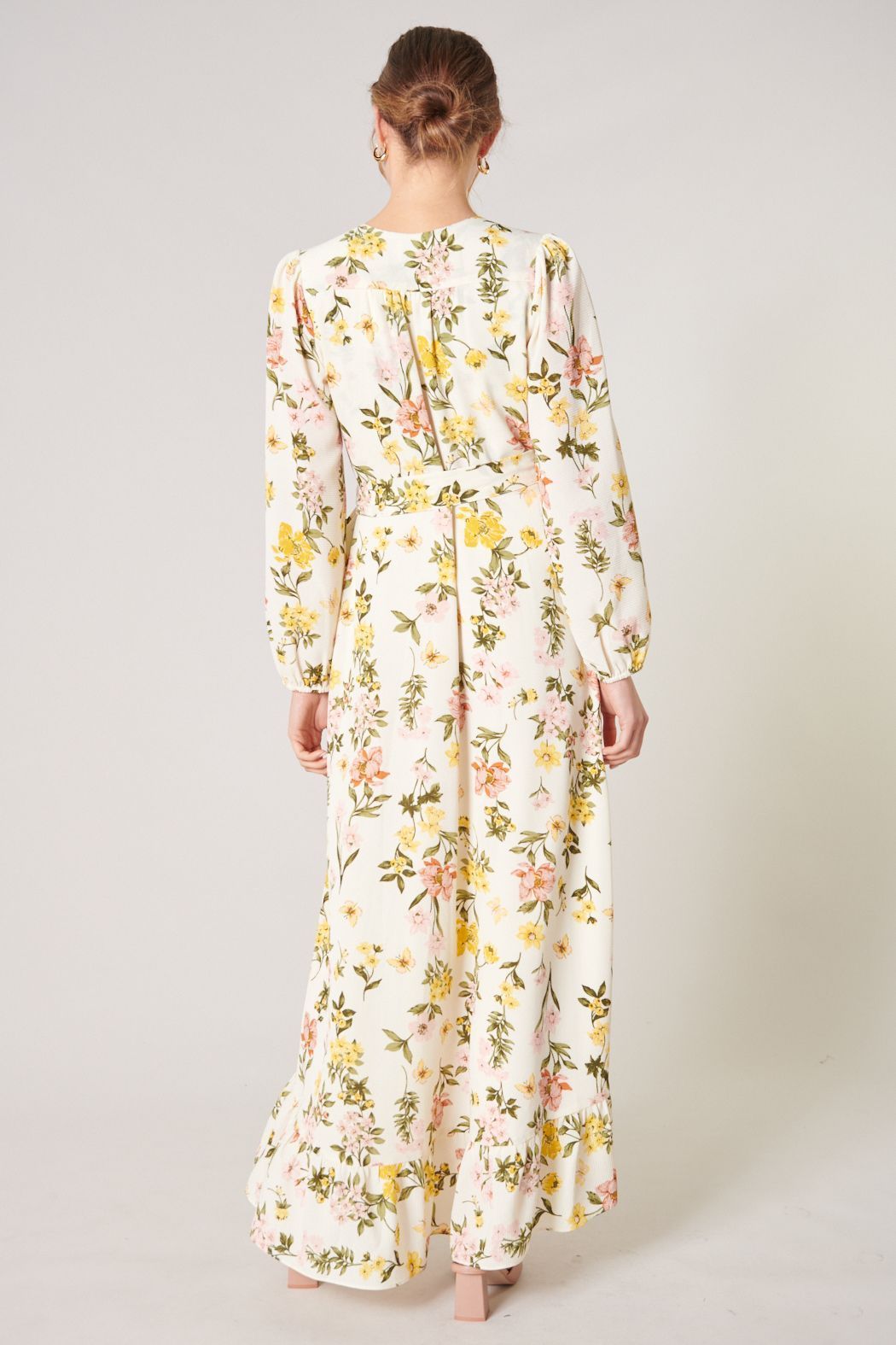 Back view of ivory floral maxi dress with long sleeves and flowing ruffle hem