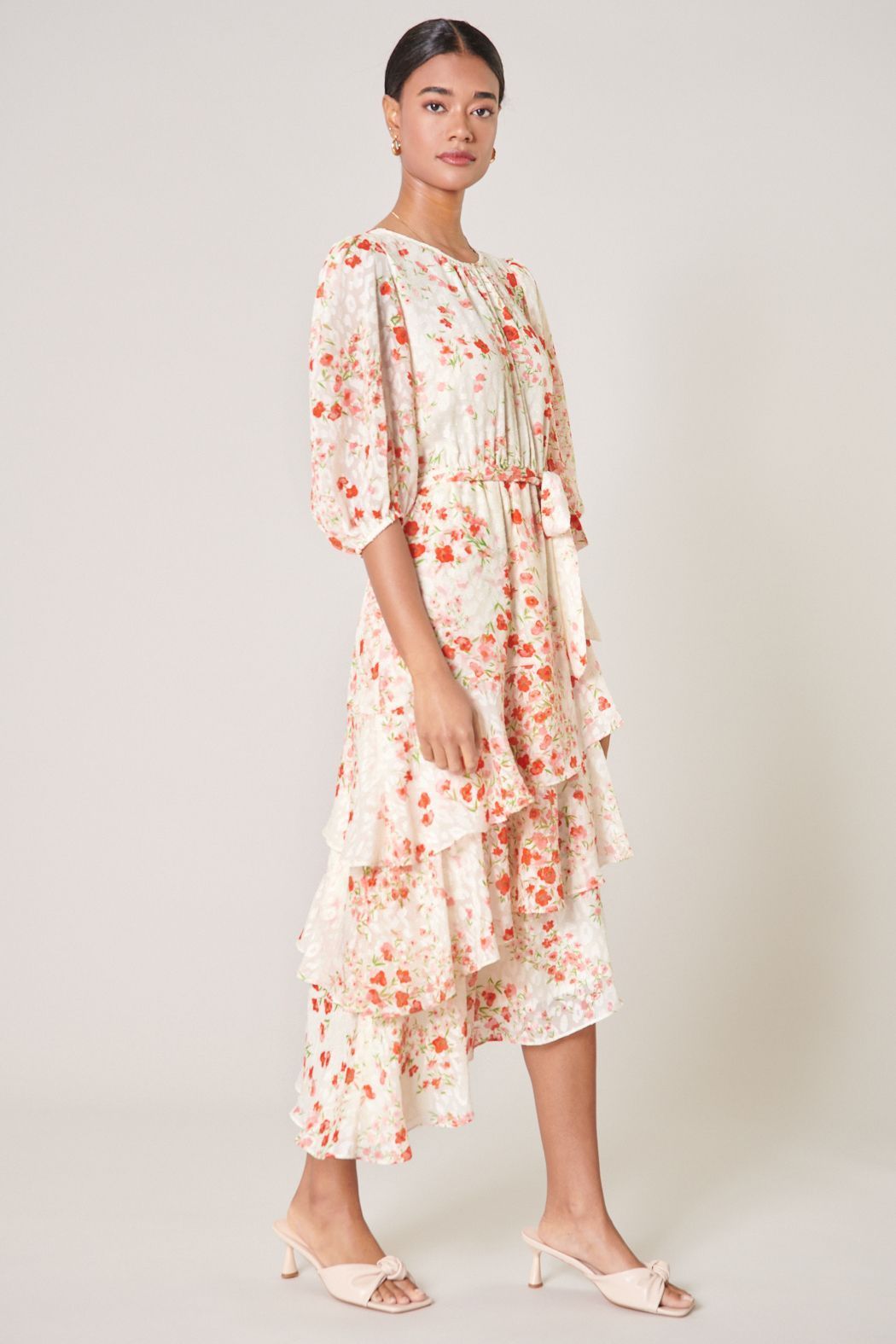 Side view of blush floral midi dress with puff sleeves and cascading ruffle hem